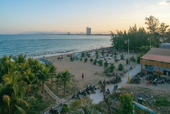 A beach with a parking area, palm trees, and a building with a red roof. - Phuc Thuan Hotel (Ninh Chu)