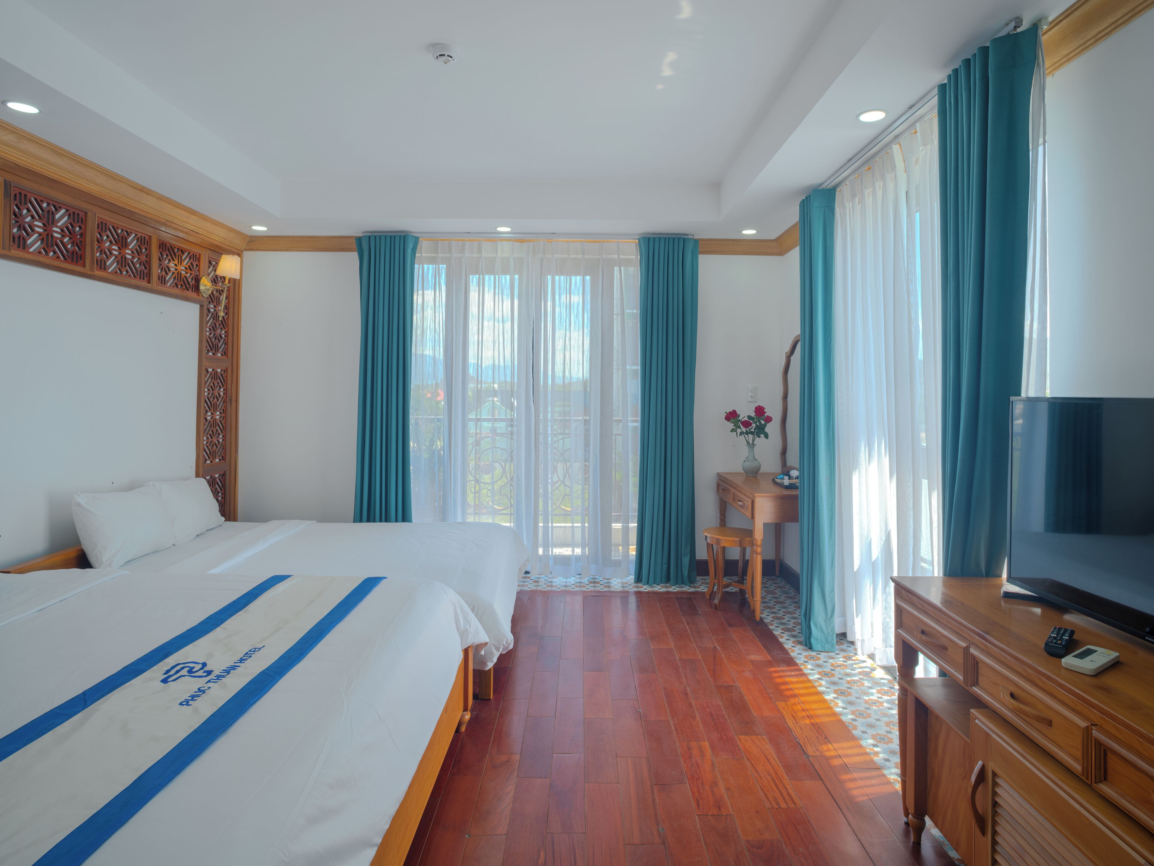 Habitación de hotel con dos camas, un aparador de madera, un televisor y un escritorio con un florero.