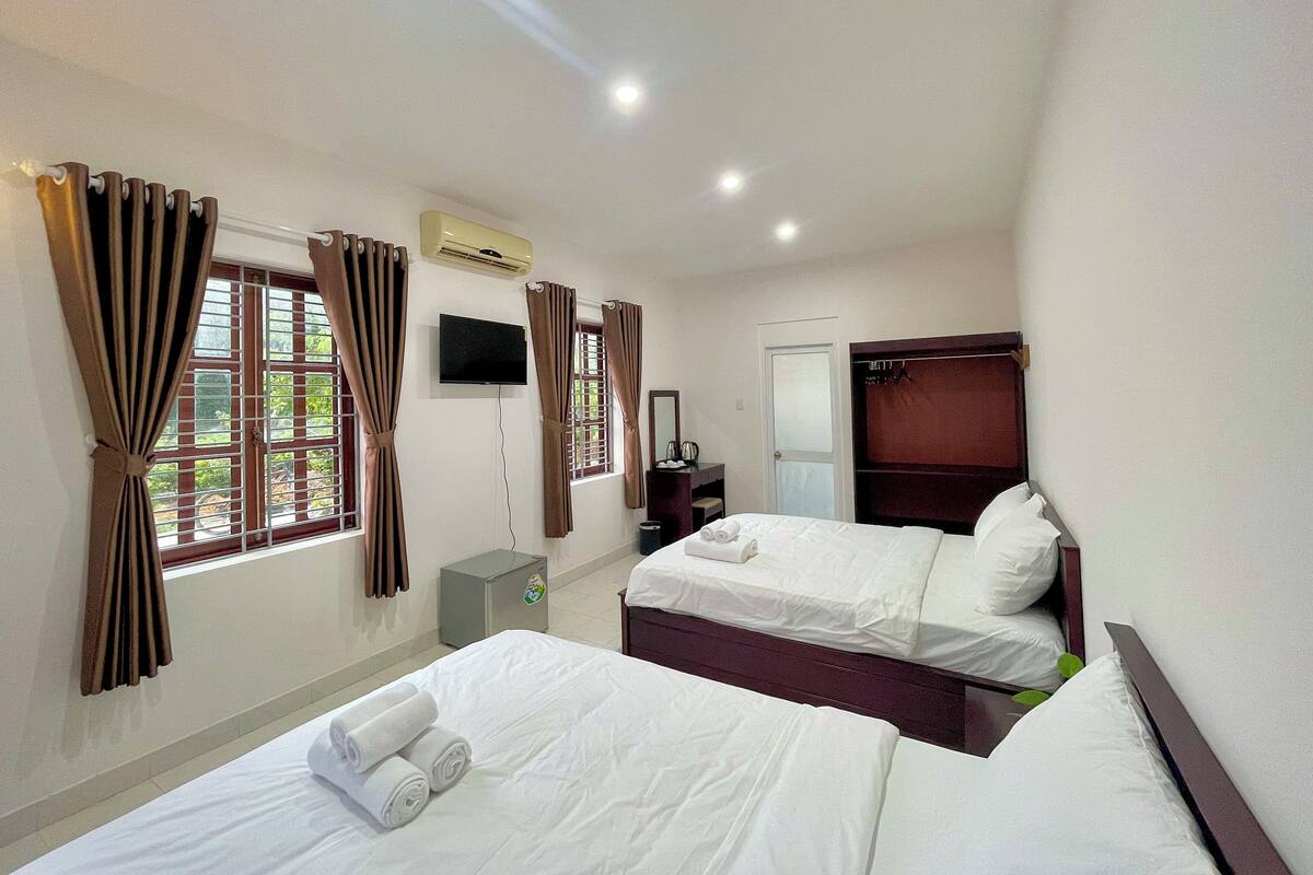 A hotel room with two beds, a TV, an air conditioner, and a window with curtains.