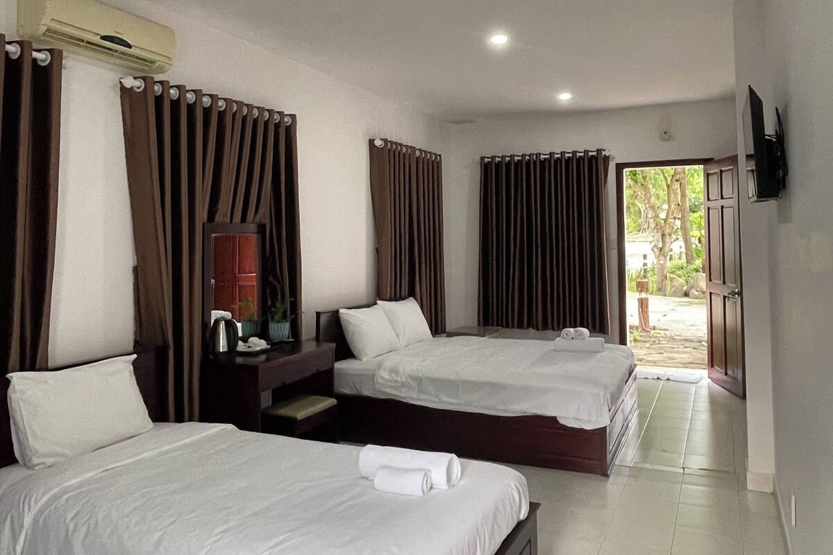 A hotel room with two beds, a TV mounted on the wall, and a large window with curtains.