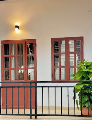 Un balcon avec une porte et des fenêtres rouges, une rambarde noire et un pot de fleurs.