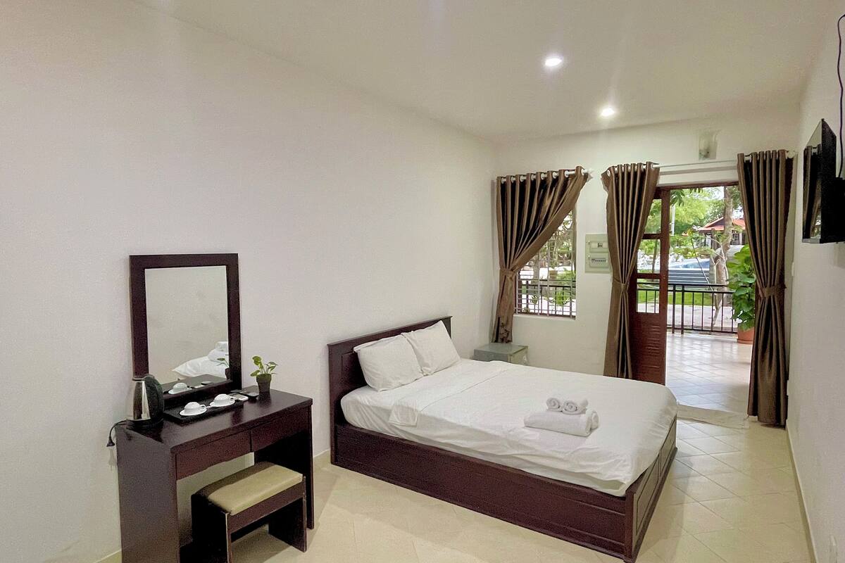 A hotel room with a bed, a bedside table, a mirror, and a window with curtains.