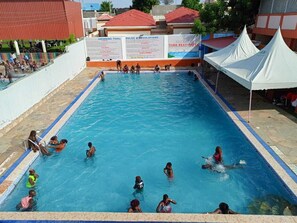 A swimming pool with people swimming and playing, surrounded by buildings and tents. - The Great Turk Reef Hotel (Lodwar)
