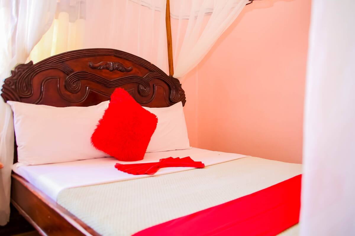 A bed with a wooden headboard, white bedding, and a red pillow.