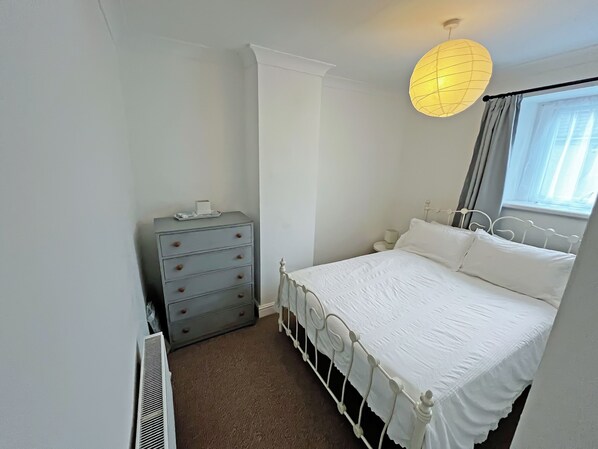 A bedroom with a bed, dresser, radiator, and a window with curtains.