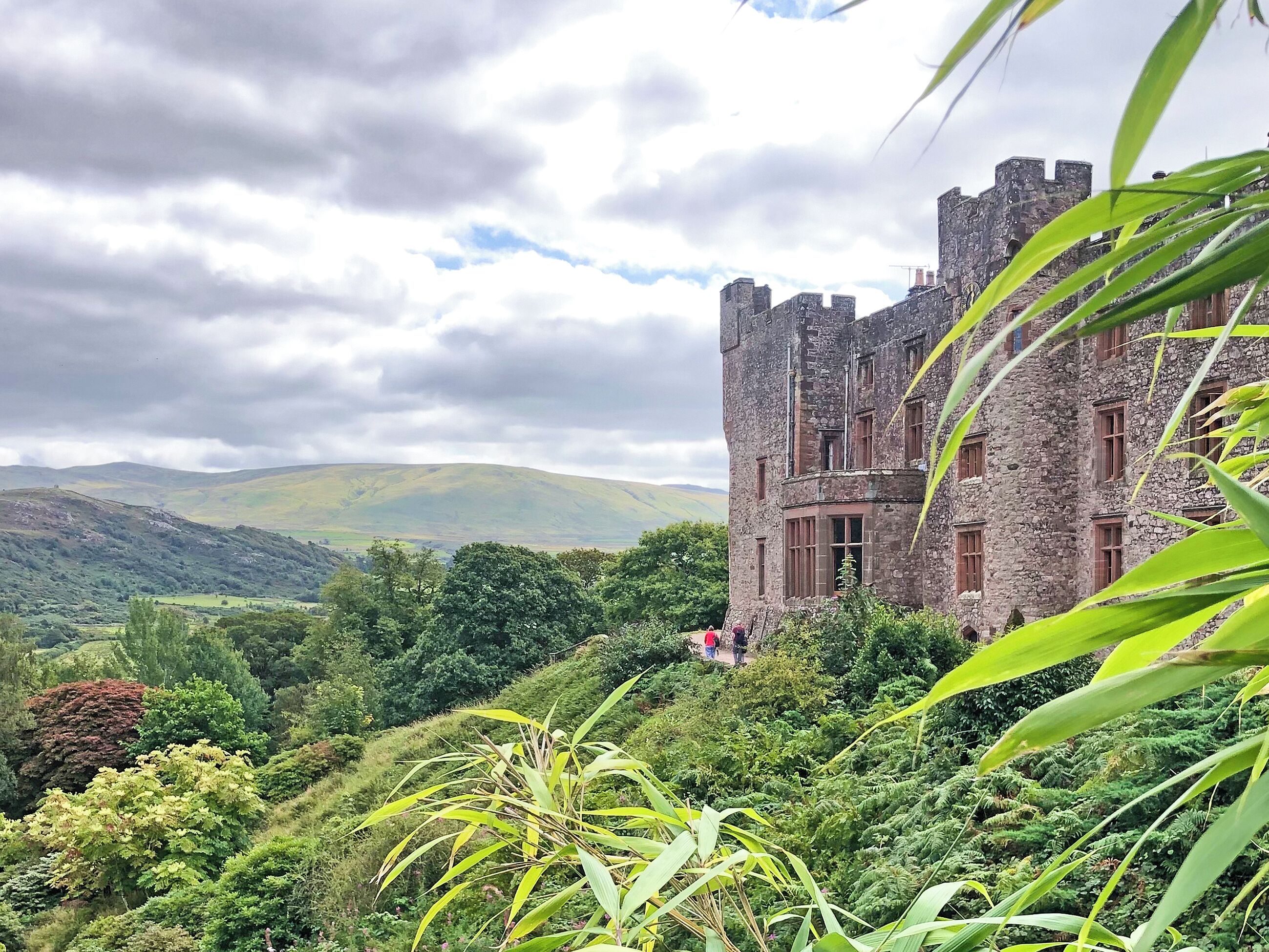 A castle with a stone exterior, surrounded by lush greenery and hills in the background.