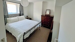 Une chambre avec un lit simple, une commode, une table de chevet, un luminaire suspendu et une fenêtre avec des rideaux.