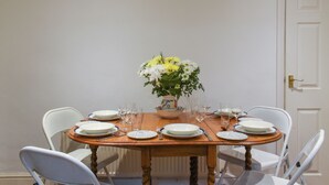 Une table à manger dressée pour six personnes, avec des chaises blanches, un vase de fleurs et divers objets en verre.