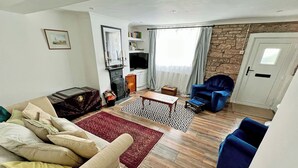 Un salon avec un canapé, des fauteuils, une cheminée, un téléviseur et un mur en pierre.