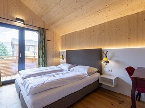 Ein Doppelbett mit weißer Bettwäsche in einem Zimmer mit Holzboden und schrägen Wänden, Blick auf ein Gebäude.