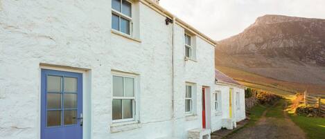 A row of white buildings with distinctively colored doors, set against a mountainous backdrop.