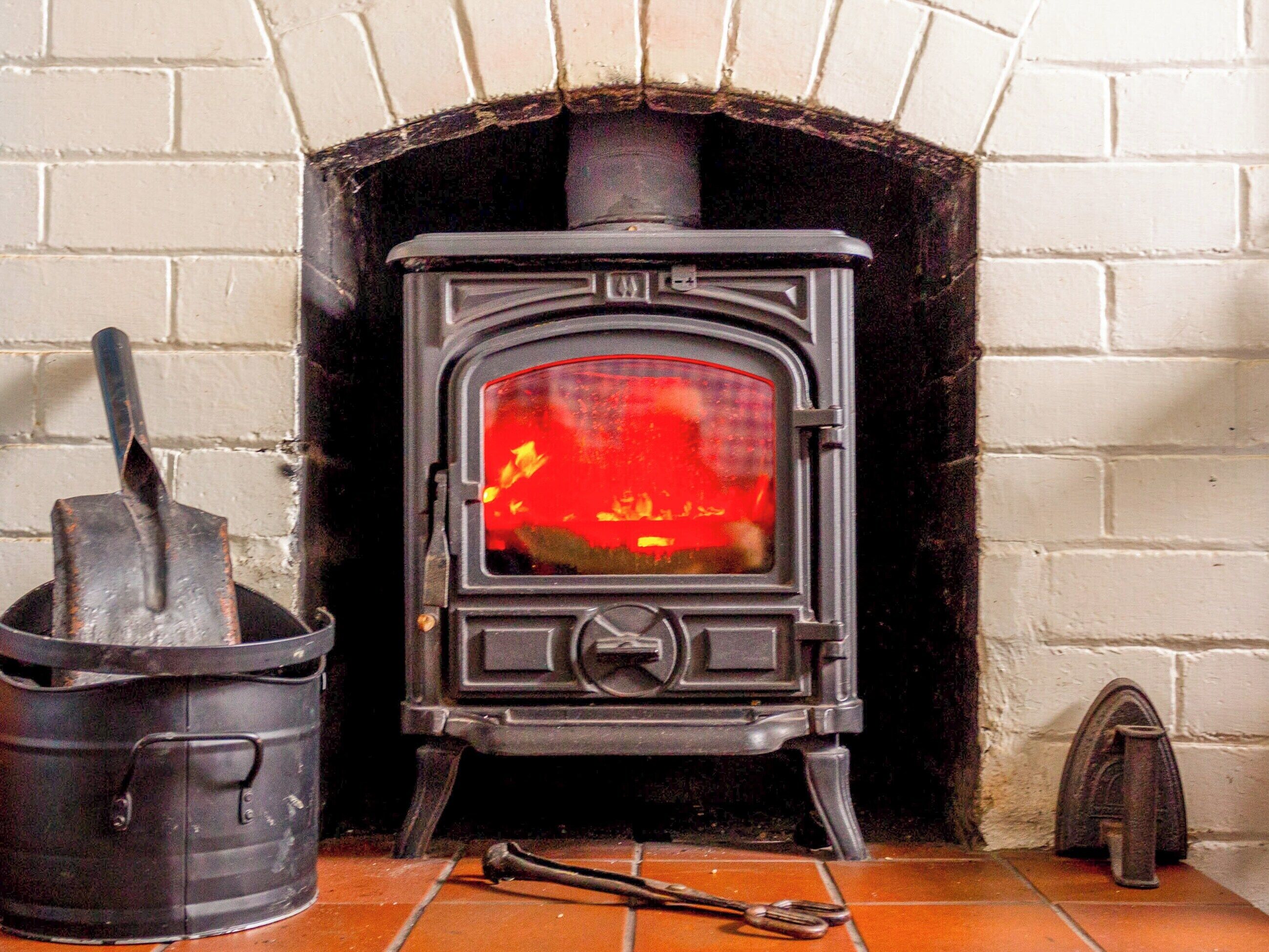 A traditional wood-burning stove with a visible fire, a metal bucket, and a pair of tongs on a tiled floor.