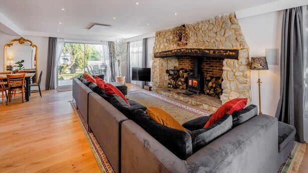 A modern living room with a stone fireplace, a large sofa, a dining area with a table and chairs, and a TV.