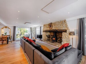 A modern living room with a stone fireplace, a large sofa, a dining area with a table and chairs, and a TV. - 8 bedroom accommodation in Bluebell Hill, near Chatham (Bluebell Hill, near Chatham)