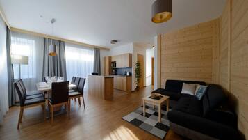 Una sala de estar moderna con sofá, mesa de comedor y sillas. Cuenta con una zona de cocina con armarios de madera y un comedor con lámpara.