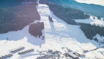 Vista aérea de una estación de esquí con varios edificios, zonas de estacionamiento y un paisaje cubierto de nieve.