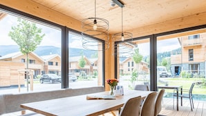 A modern dining area with a wooden table and chairs, large windows with a view of a mountain landscape, and a hanging light fixture. - Spacious Apartment With Pool (Sankt Georgen am Kreischberg)