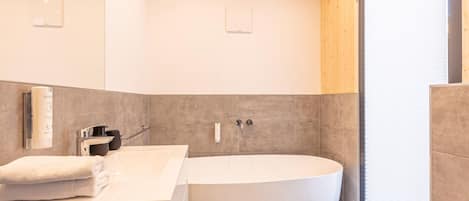 A modern bathroom with a freestanding bathtub, a vanity with a towel, and a window with blinds.