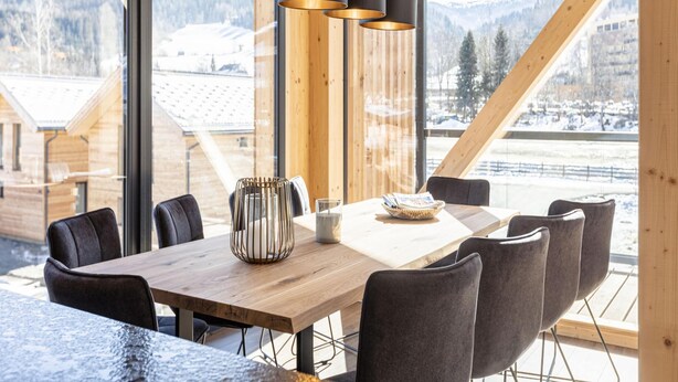 Un interior de madera con una gran mesa de comedor, sillas negras y vistas a montañas nevadas a través de amplios ventanales.