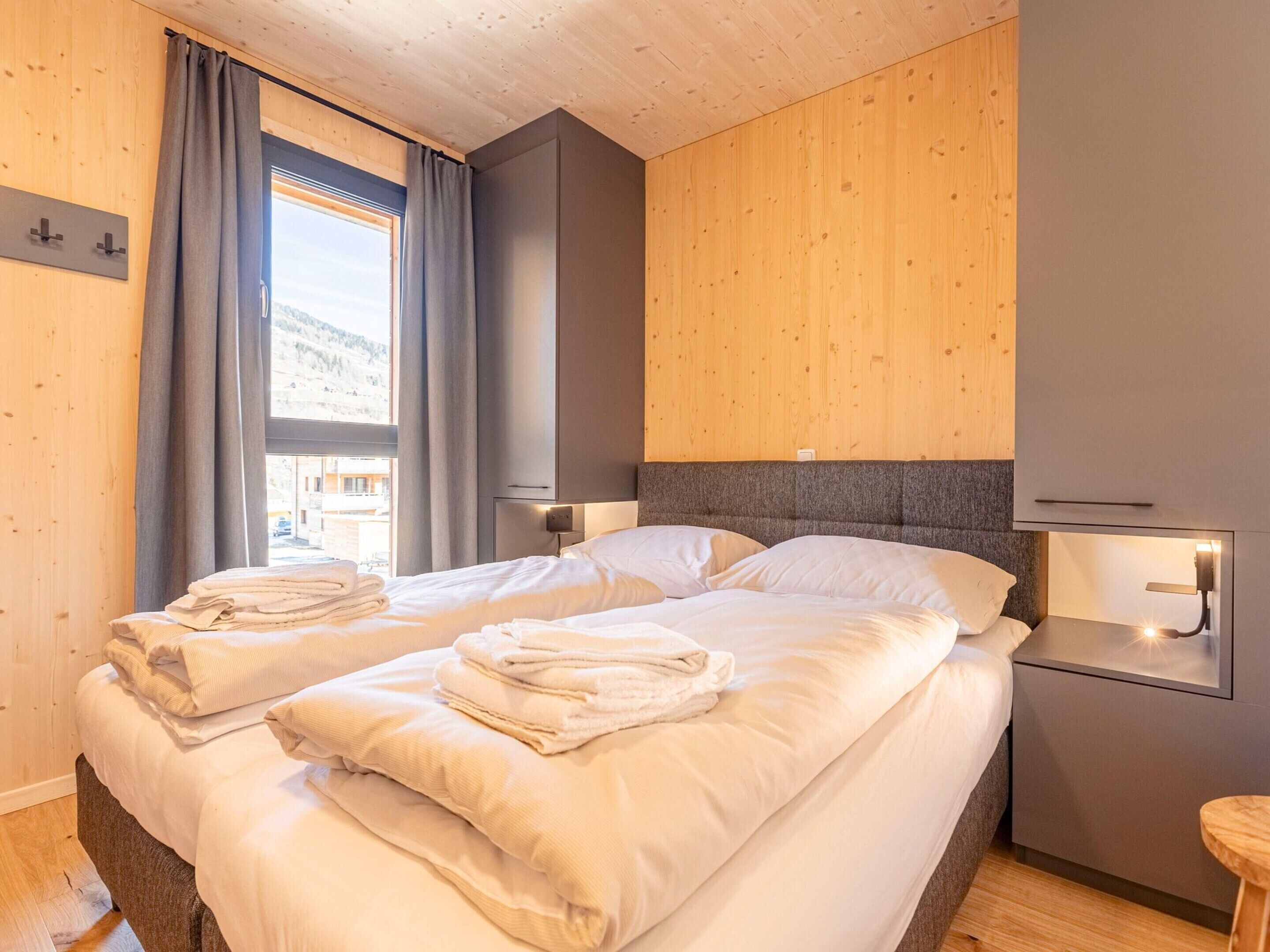 Una habitación de hotel moderna con dos camas, paredes de paneles de madera, un ventanal con cortinas y lámparas de noche.
