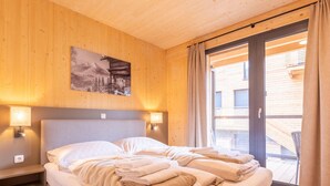 A double bed with a headboard, two bedside lamps, a window with curtains, and a wooden ceiling. - Lovely Penthouse With Sauna (Sankt Georgen am Kreischberg)