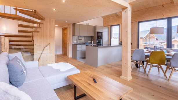 A modern interior with a wooden staircase, a kitchen, and a dining area with a view. - Lovely Penthouse With Sauna (Sankt Georgen am Kreischberg)