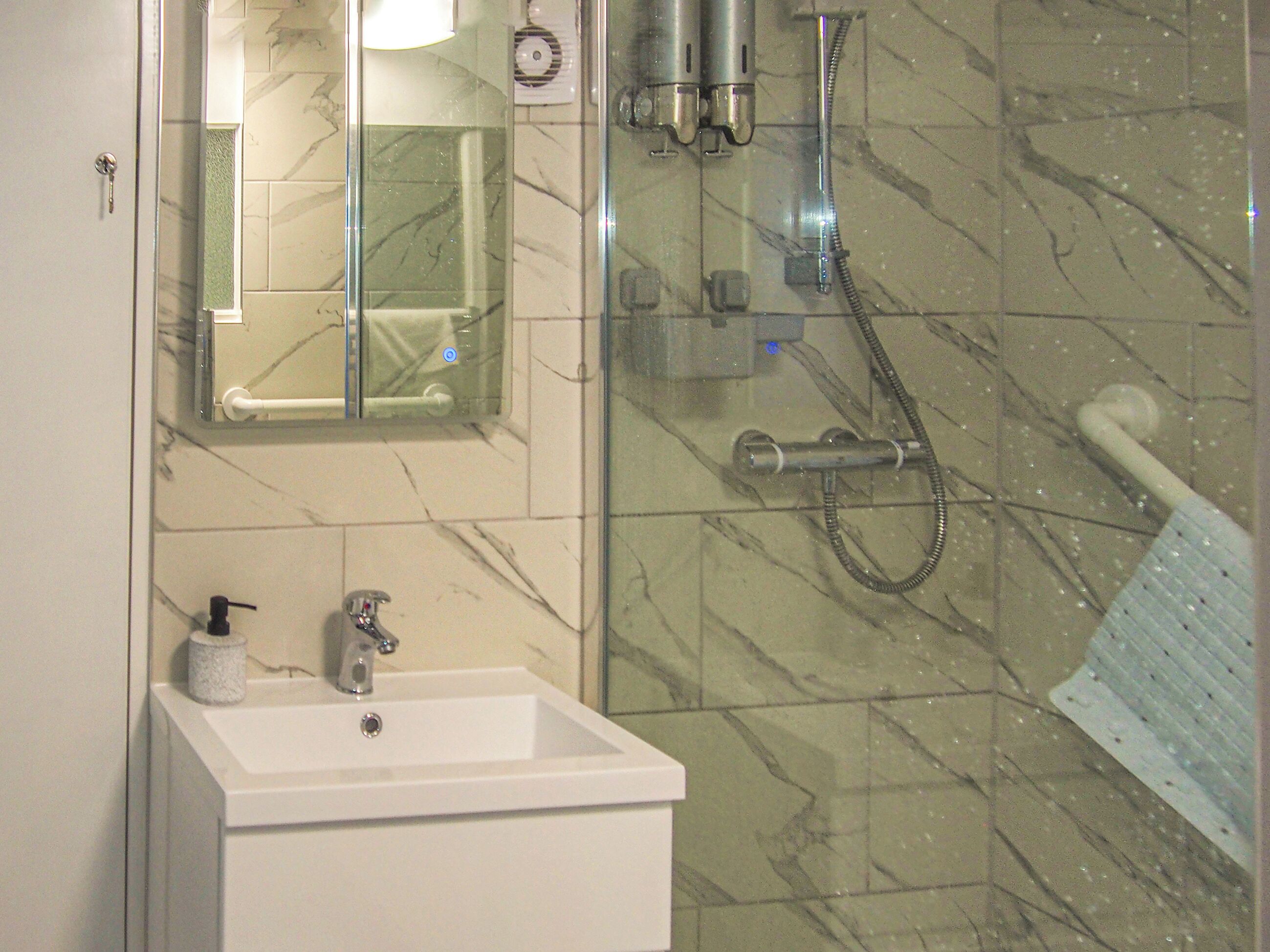 Un baño con lavamanos blanco, cabina de ducha de vidrio y pared revestida de mármol.