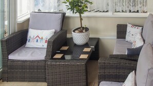 A cozy seating area with wicker furniture, a potted plant, and a window with lace curtains. - 3 bedroom accommodation in Pagham, near Bognor Regis (Pagham, near Bognor Regis)