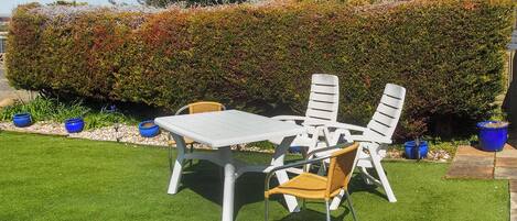Een terras met een tafel en stoelen, omgeven door een verzorgde haag en blauwe plantenbakken.