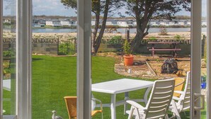 A patio with a white table and chairs, a bird sculpture, and a view of a lake with houses in the background. - 3 bedroom accommodation in Pagham, near Bognor Regis (Pagham, near Bognor Regis)