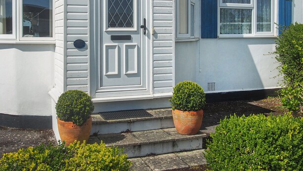 A white house with a front door, two windows, and a blue door. There are two potted plants in front of the house. - 3 bedroom accommodation in Pagham, near Bognor Regis (Pagham, near Bognor Regis)