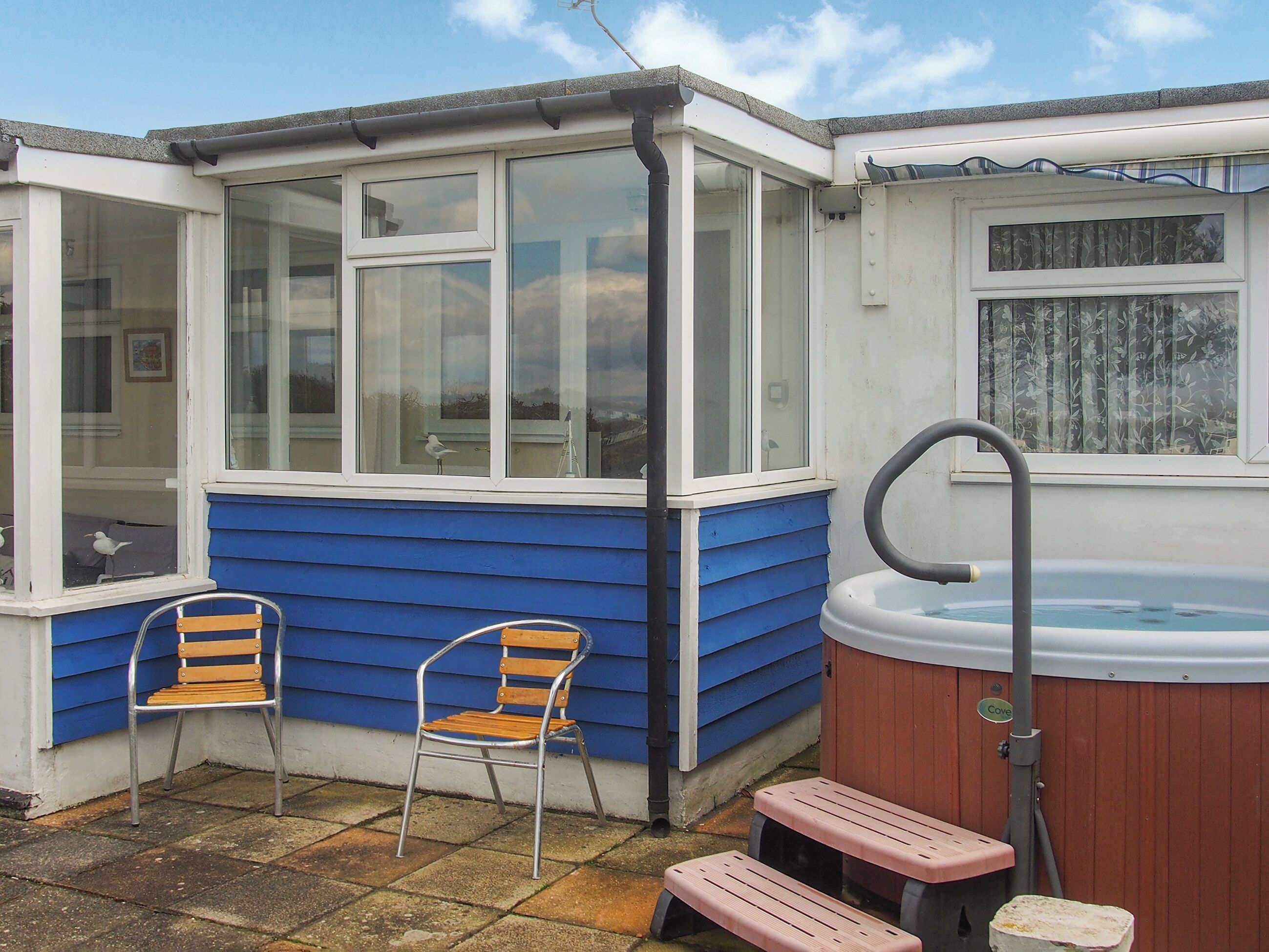 A small, enclosed patio area with a hot tub, two wooden chairs, and a wooden bench.