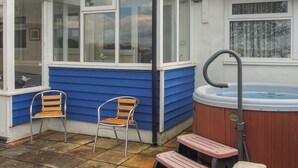 A small, enclosed patio area with a hot tub, two wooden chairs, and a wooden bench. - 3 bedroom accommodation in Pagham, near Bognor Regis (Pagham, near Bognor Regis)