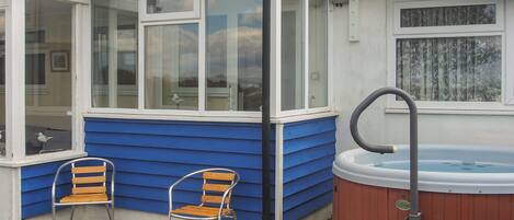 A small, enclosed patio area with a hot tub, two wooden chairs, and a wooden bench.