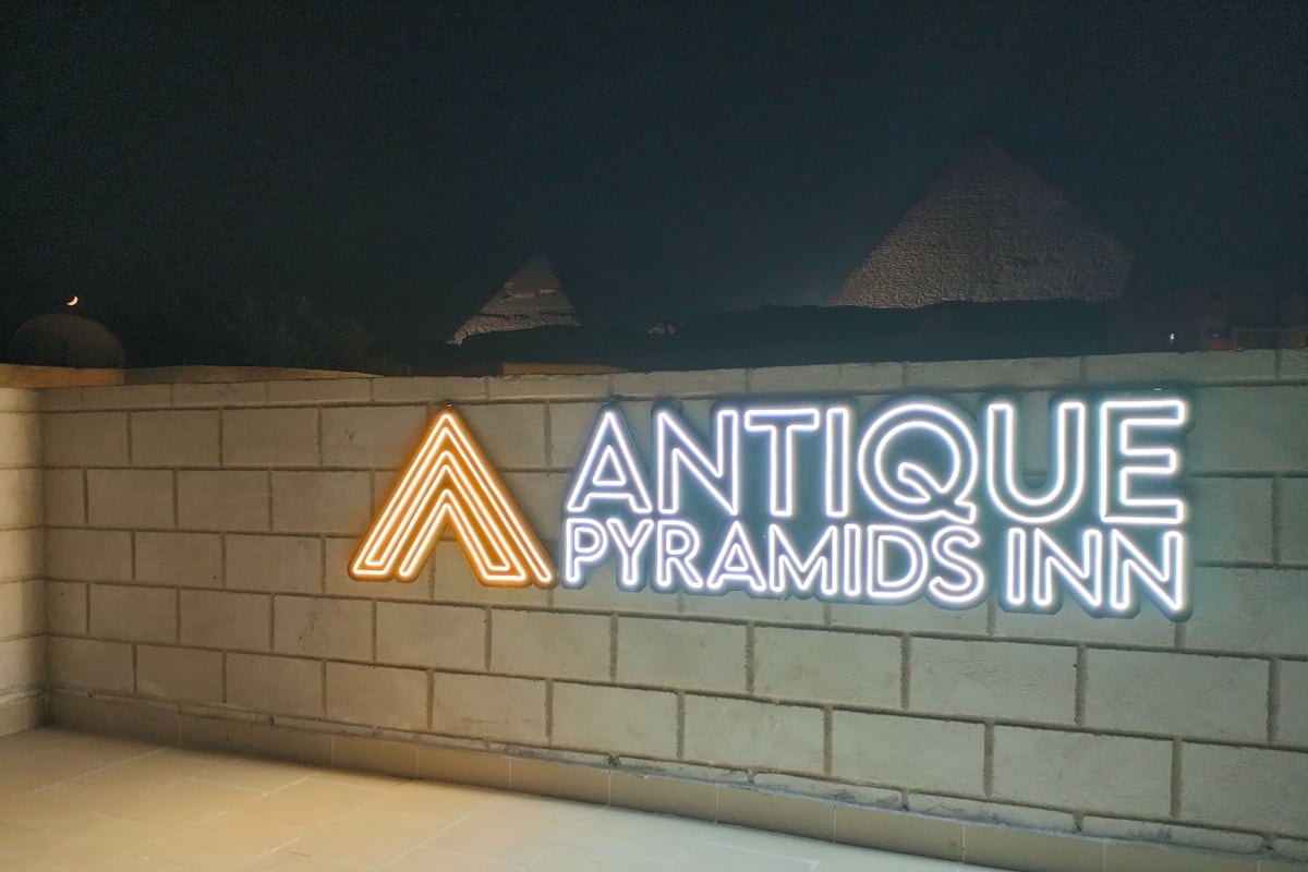A neon sign for 'Antique Pyramids Inn' on a brick wall.