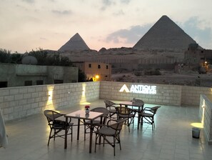 A rooftop terrace with tables and chairs, a sign for 'ANTIQUE', and views of pyramids. - Antique Pyramids Inn (Giza)