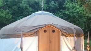 A round, wooden yurt with a conical roof, two circular doorways, and wooden posts at the entrance. - 1 bedroom accommodation in Bishopsteignton (Bishopsteignton)