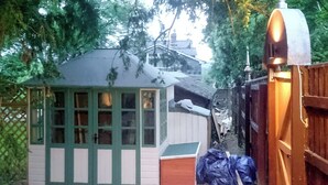 A small, single-story shed with a sloped roof and multiple windows, surrounded by a wooden fence and gravel ground. - 1 bedroom accommodation in Bishopsteignton (Bishopsteignton)