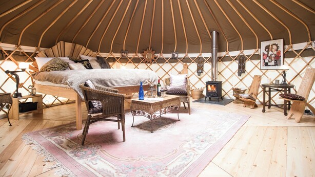 A cozy interior of a yurt with a bed, wicker furniture, a rug, and a wood-burning stove. - 1 bedroom accommodation in Bishopsteignton (Bishopsteignton)