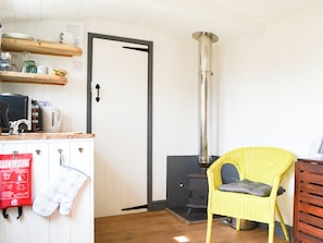 A cozy room with a kitchenette, a yellow wicker chair, a fireplace, and a fire blanket on the wall.