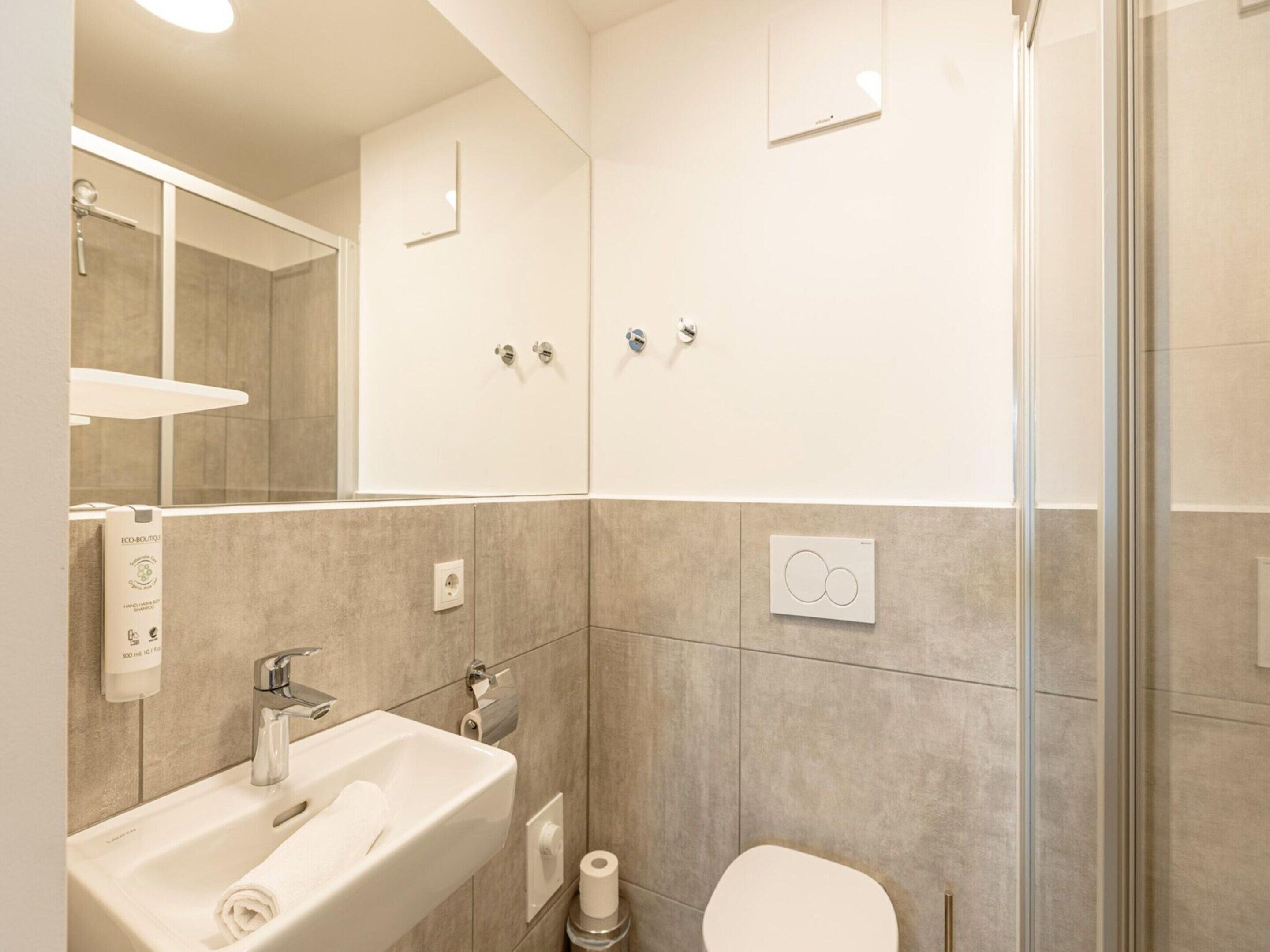 A modern bathroom with a sink, mirror, toilet, and shower.