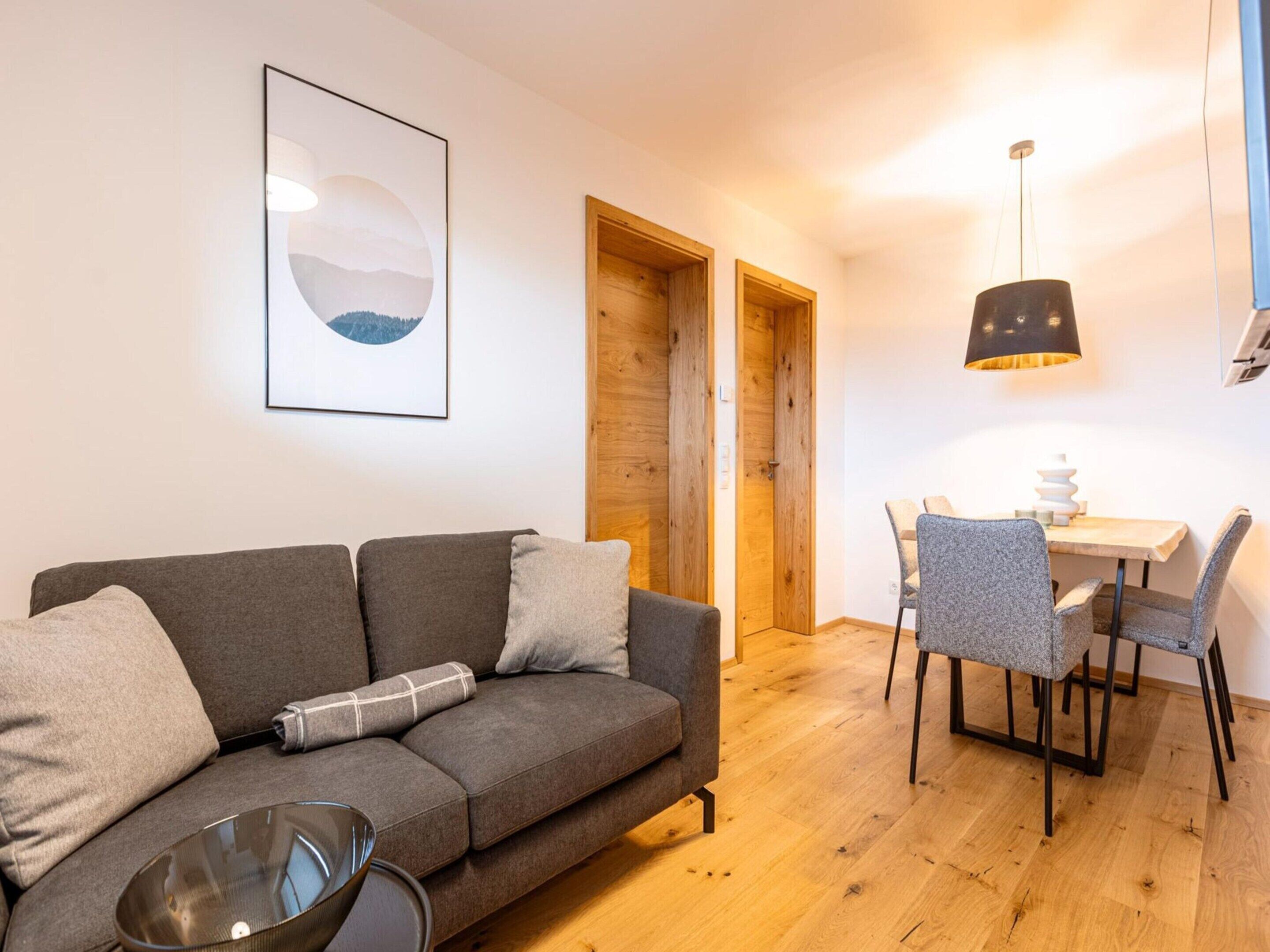 Een moderne woonkamer met een grijze bank, een eettafel met stoelen en een houten deur.