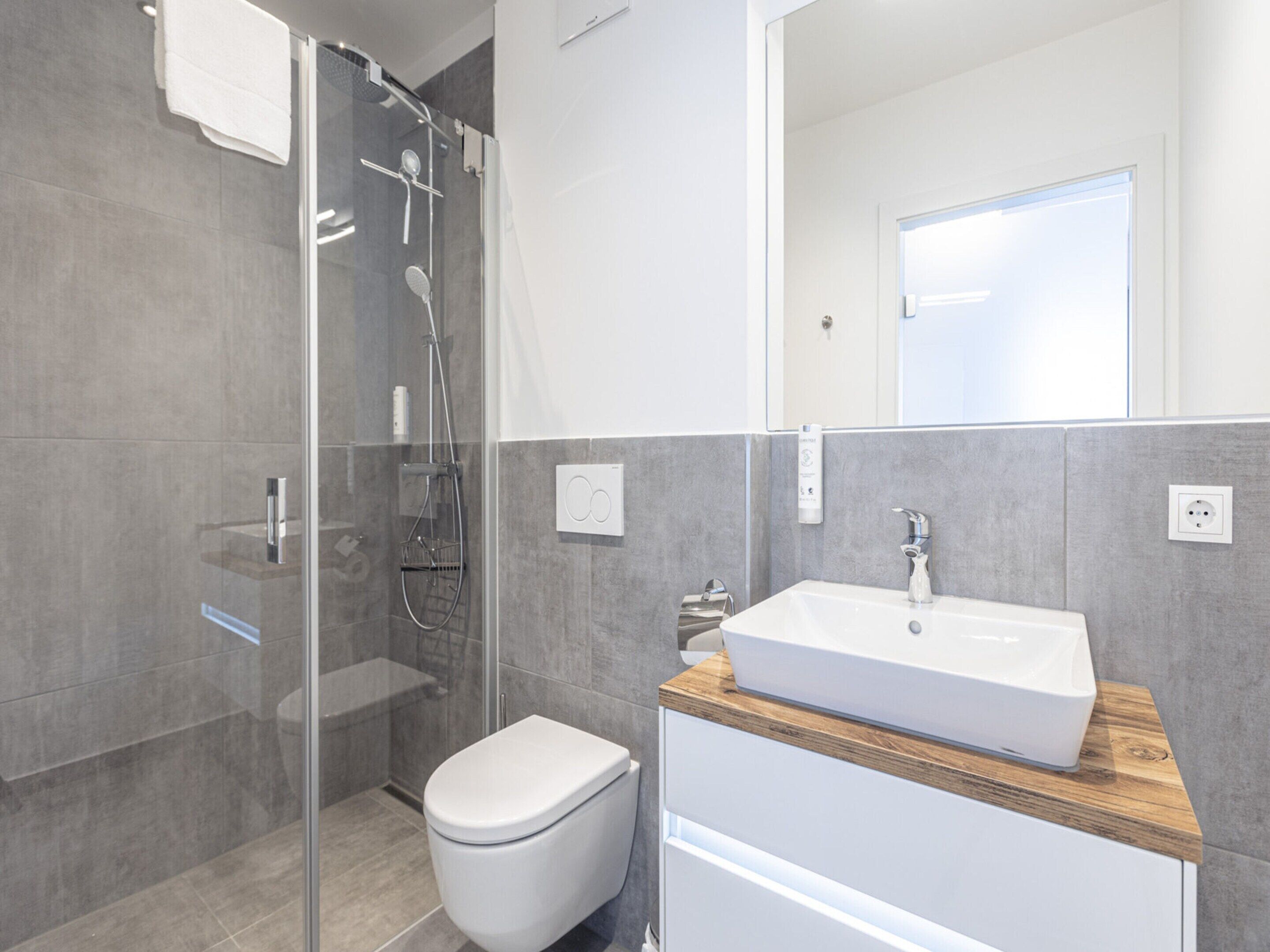 Une salle de bain moderne avec une douche à parois de verre, des toilettes blanches et un meuble-lavabo en bois avec un vasque blanche.
