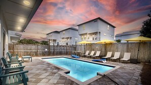 A swimming pool with lounge chairs and umbrellas, surrounded by a wooden fence and houses in the background. - Seabbatical: Private heated pool, Free golf cart, 2min to beach, Game room (Miramar Beach)