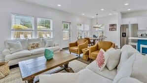 A spacious living room with a white sofa, a wooden coffee table, and a dining area with a table and chairs. - Seabbatical: Private heated pool, Free golf cart, 2min to beach, Game room (Miramar Beach)