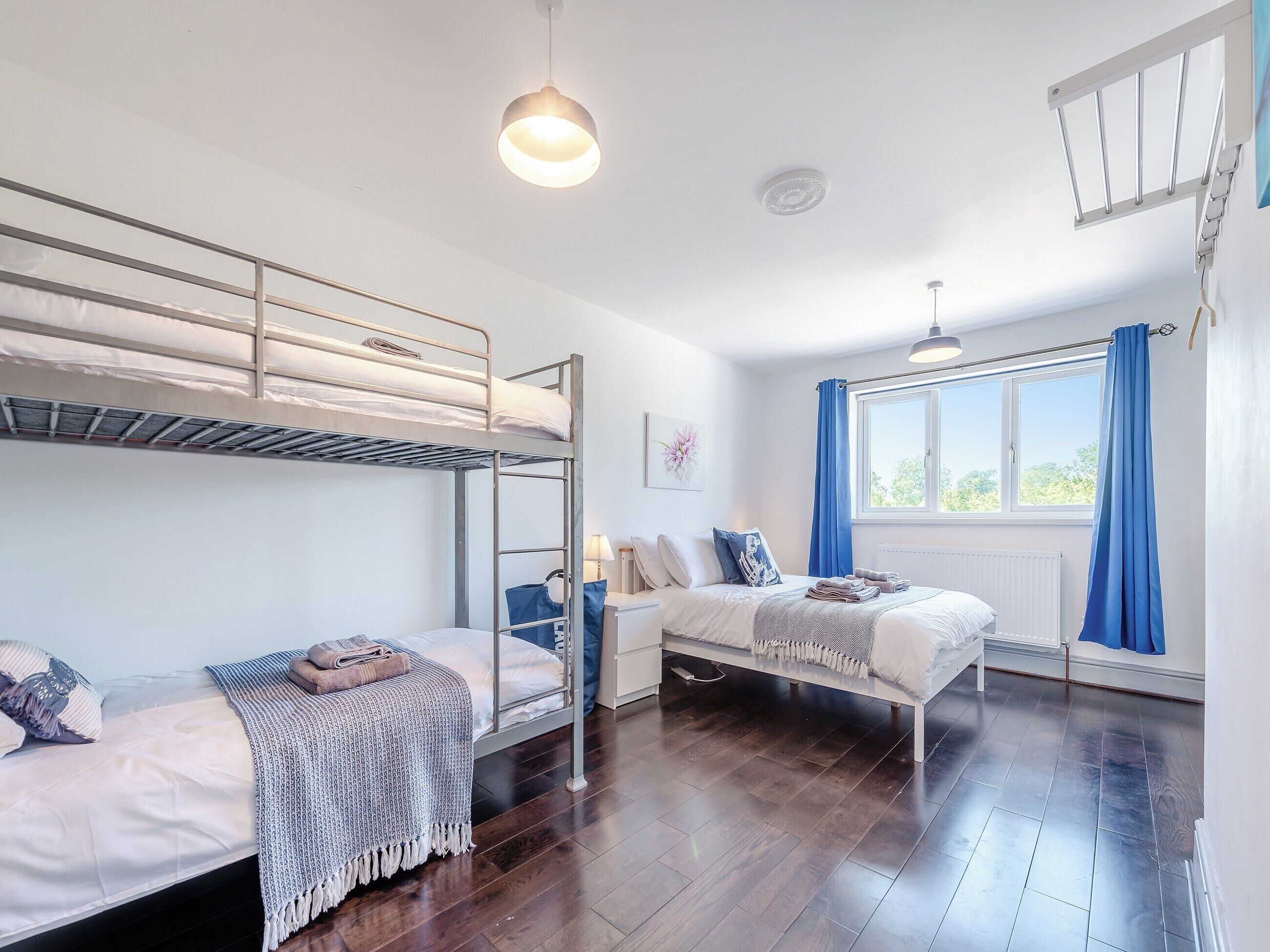 A room with bunk beds, a window with curtains, a radiator, and a hanging light fixture.
