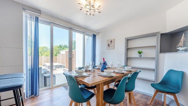 A dining area with a wooden table, teal chairs, and a view of the outdoors through large sliding glass doors. - 5 bedroom accommodation in Eglwyswrw (Eglwyswrw)