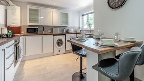A modern kitchen with white cabinets, a built-in microwave, and a dining area with a wooden table and chairs. - 5 bedroom accommodation in Eglwyswrw (Eglwyswrw)