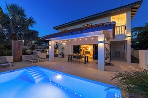 A modern house with a swimming pool, outdoor seating, and string lights.