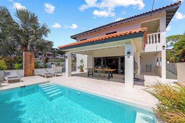 A modern house with a swimming pool, outdoor seating, and a covered patio area.
